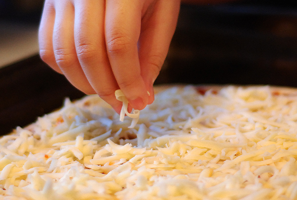 Mica adding cheese to her pizza.