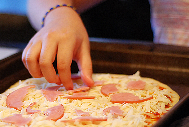 Mica adding pepperoni to her pizza.